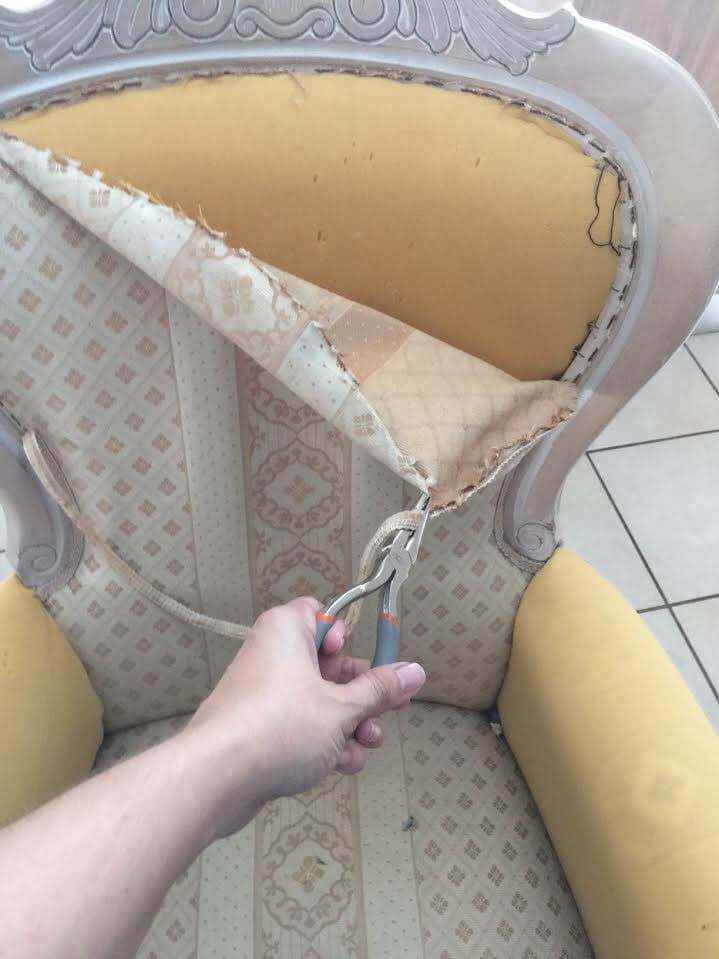 hand removing the fabric of a victorian arm chair to reupholster it